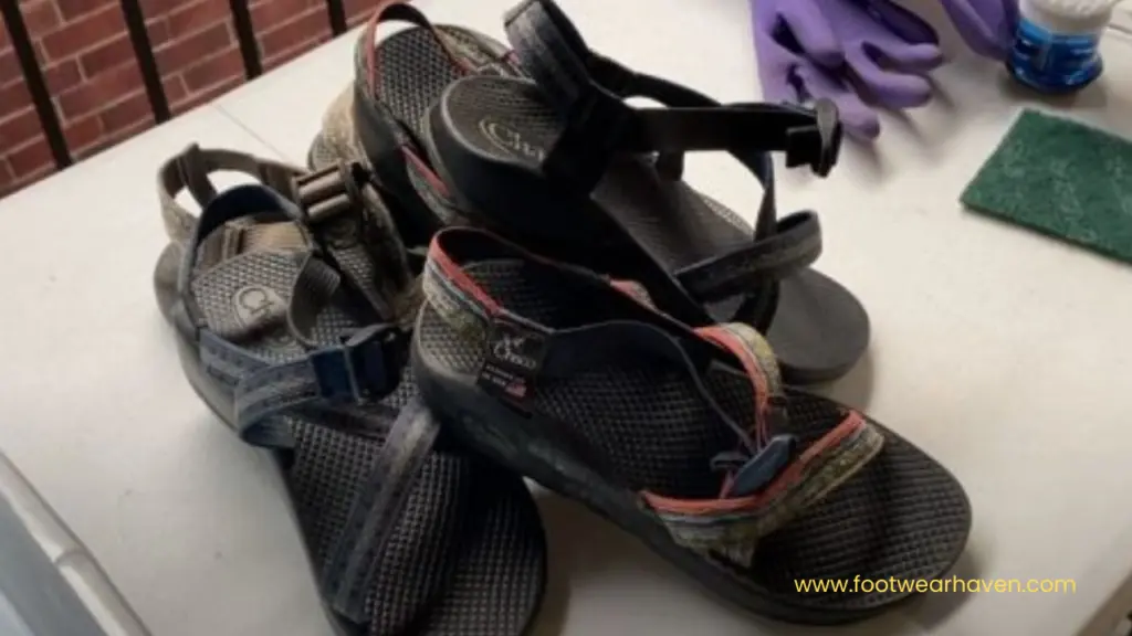 A pair of well-worn sandals with colorful straps rests on a table, next to cleaning supplies and purple gloves.